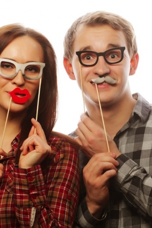 people, party, love and leisure concept - lovely couple holding party glasses and mustaches on stick